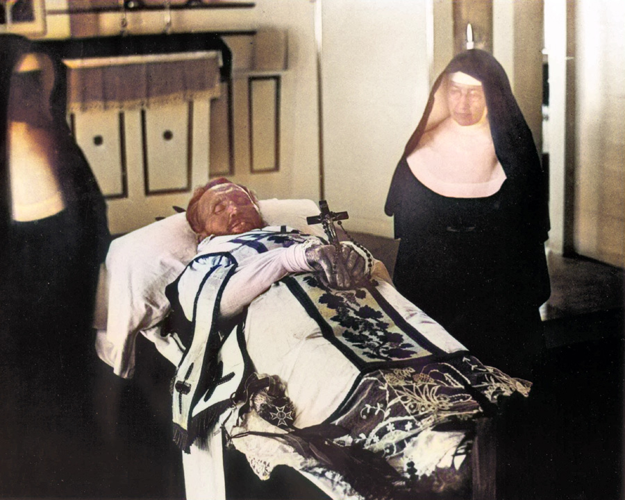 St. Damien de Veuster and St. Marianne Cope standing beside Father Damien's funeral bier
